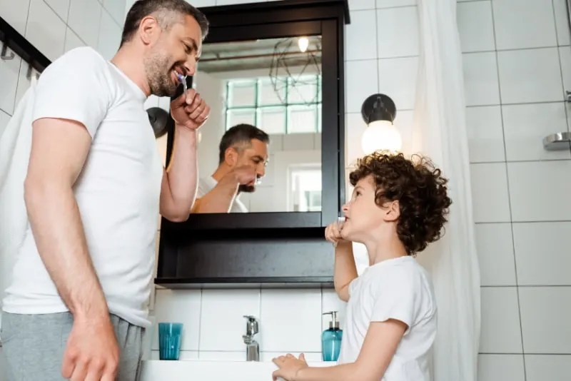 Hubscher-Vater-und-lockiger-Sohn-die-Zahne-im-Badezimmer-putzen