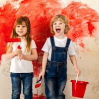 Kinder Maler. Kleine Künstler mit einem Pinsel in der Hand und einem Farbroller mit roter Farbe auf der Tapete im Raum an der Wand.