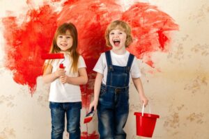 Kinder Maler. Kleine Künstler mit einem Pinsel in der Hand und einem Farbroller mit roter Farbe auf der Tapete im Raum an der Wand.
