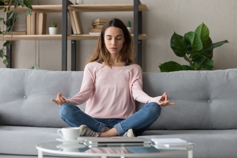 Ruhige-Frau-entspannen-sich-auf-der-Couch-und-meditieren-beim-Uben-von-Yoga