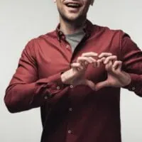 Teilansicht des fröhlichen Mannes, der Herzzeichen mit den Händen lokalisiert auf grauem, menschlichem Gefühl und Ausdruckskonzept zeigt