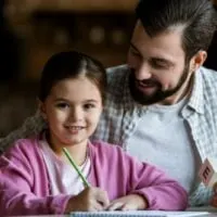 Vater mit Tochter sitzt am Tisch mit Würfelbuchstaben und Zeichnung