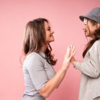 Die entzückende Mama sitzt neben ihrer süßen lächelnden Tochter und spielt mit ihr Patty-Cake ein Klatschspiel