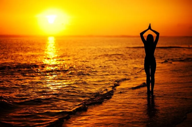 Frau-praktiziert-Yoga-bei-Sonnenuntergang-an-der-Kuste