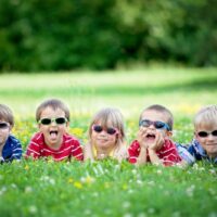 Fünf entzückende Kinder, die im Gras liegen, lächeln und Spaß haben