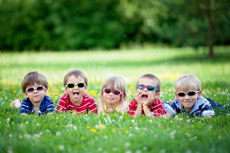 Fünf entzückende Kinder, die im Gras liegen, lächeln und Spaß haben