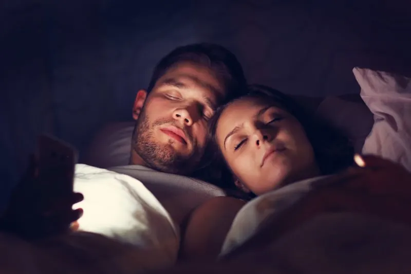 Junges-Paar-mit-Smartphones-im-Bett