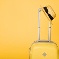 Leuchtend gelbe Reisetasche und Strohhut auf gelbem Hintergrund