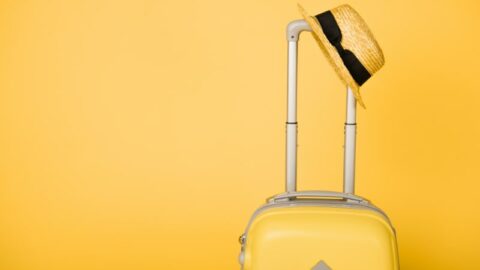 Leuchtend gelbe Reisetasche und Strohhut auf gelbem Hintergrund