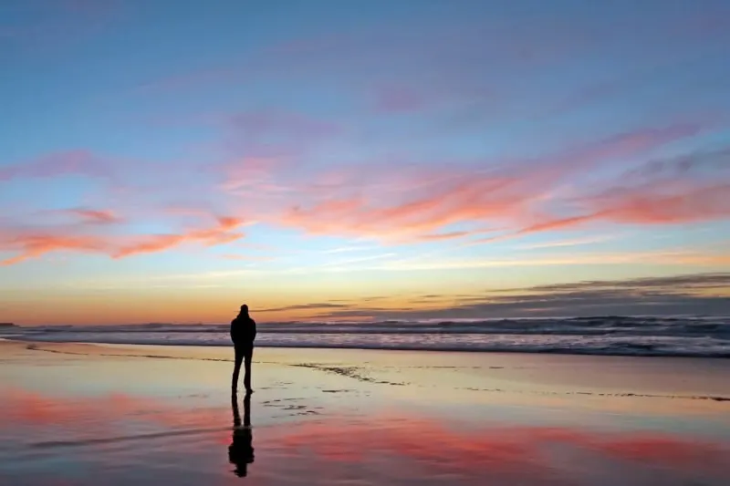 Mann, der schönen Sonnenuntergang am Strand betrachtet