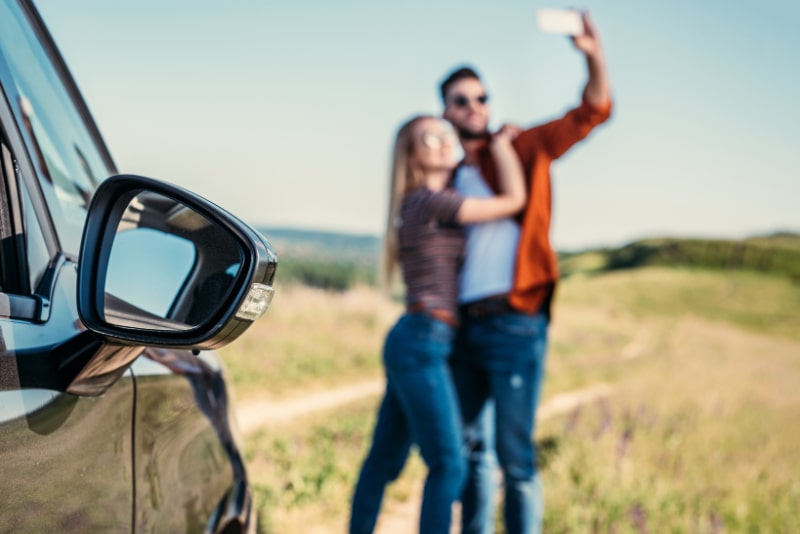 Nahaufnahme-des-Seitenspiegels-des-Autos-und-des-Paares-das-Selfie-auf-unscharfem-Hintergrund-macht