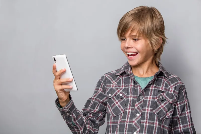 Netter-Teenager-mit-Handy-auf-grauem-Hintergrund-isoliert-Fokus-auf-Telefon