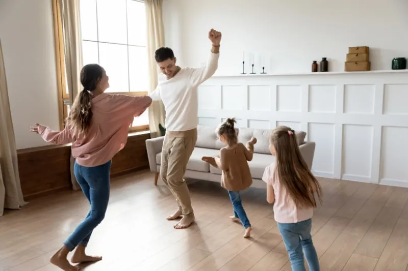 Lustige-aktive-Eltern-und-Kindertochter-tanzen-im-Wohnzimmer