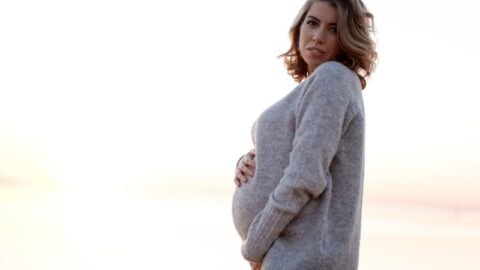 Schwangere Frau in einem Pullover, die ihren Bauch hält