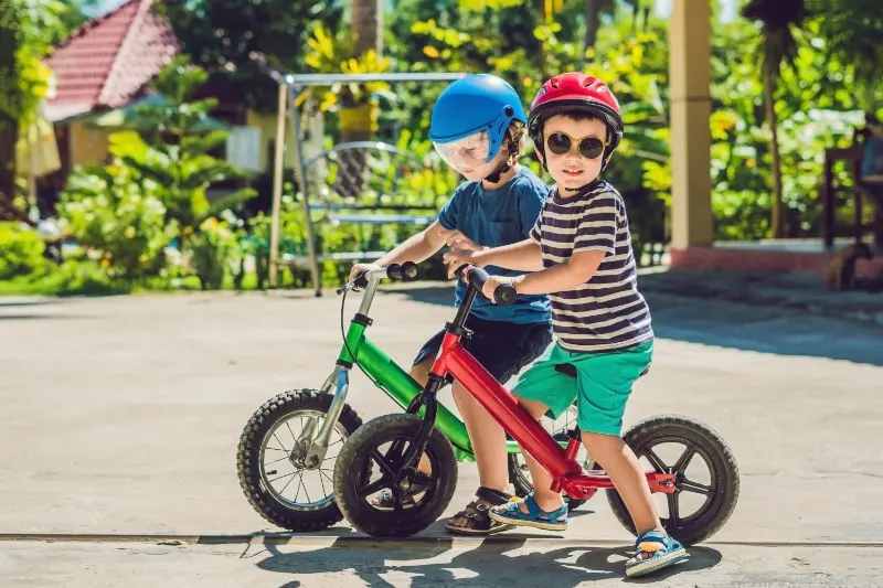 Zwei-kleine-Jungen-die-Spas-auf-dem-Laufrad-auf-einer-tropischen-Landstrase-haben.