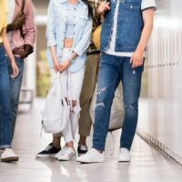 Abgeschnittene Aufnahme von jungen, stilvollen Studenten, die im College-Korridor zusammenstehen
