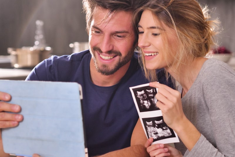 Ein-verliebtes-Ehepaar-ruft-seine-Eltern-per-Videotelefonie-uber-ein-Tablet-an-um-die-Geburt-ihres-Sohnes-mit-Ultraschall-anzukundigen.-Konzept-von-Familie-Geburt-Leben-Liebe