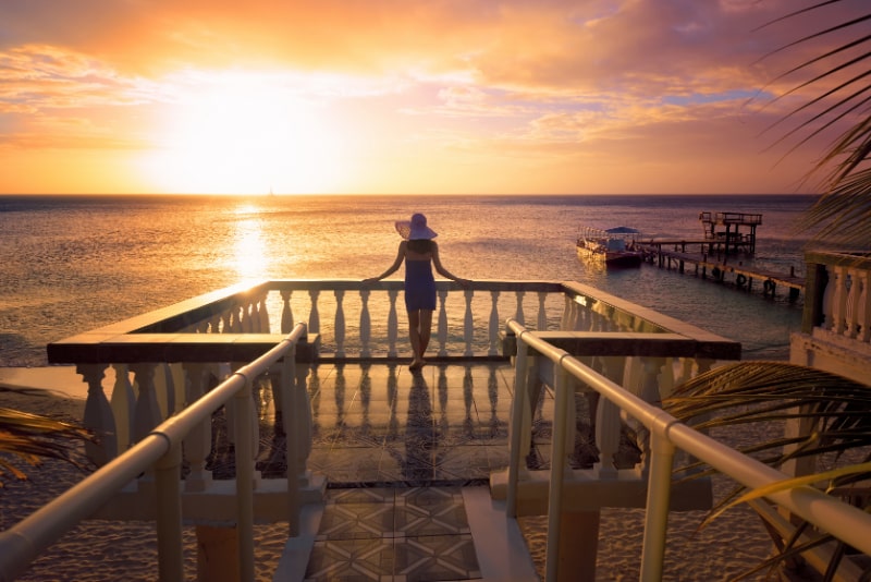 Eine-Frau-mit-Hut-die-den-romantischen-karibischen-Sonnenuntergang-betrachtet-wahrend