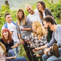 Fröhliche Freunde, die Spaß im Freien haben - Junge Leute, die zur Erntezeit Rotwein im Weingut des Bauernhauses trinken - Jugendfreundschaftskonzept mit Freunden