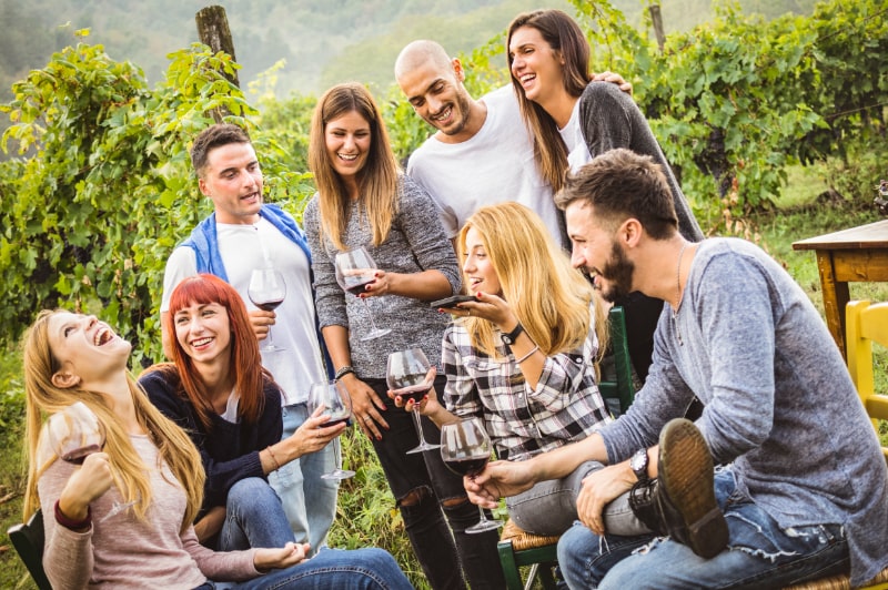 Fröhliche Freunde, die Spaß im Freien haben - Junge Leute, die zur Erntezeit Rotwein im Weingut des Bauernhauses trinken - Jugendfreundschaftskonzept mit Freunden