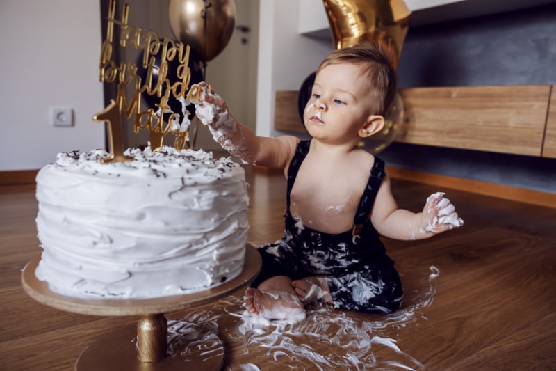 Suses-kleines-Baby-das-auf-dem-Boden-sitzt-und-an-seinem-ersten-Geburtstag-mit-seinem-Kuchen-spielt