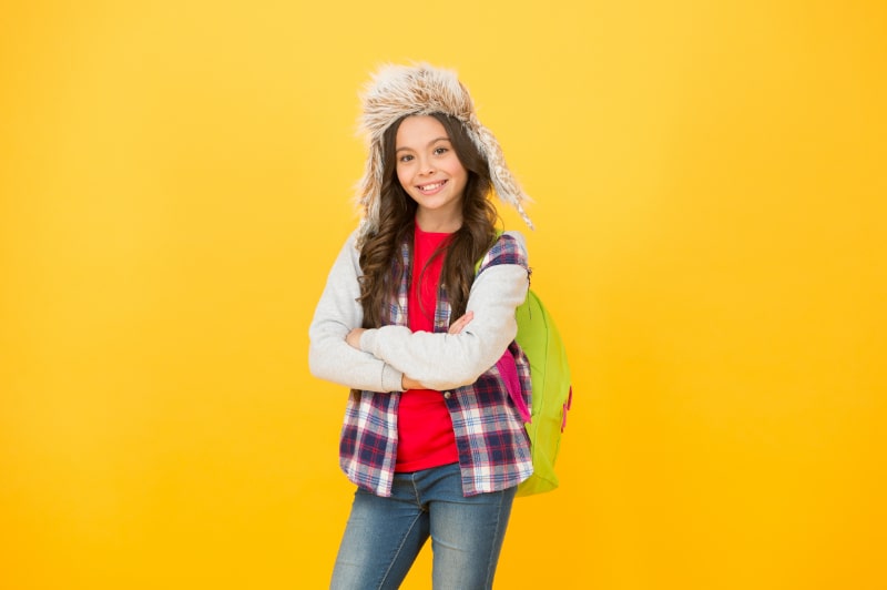 Winterveranstaltungen in der Schule. kleines Mädchen trägt Ohrenklappenhut. Winterschulzeit und Ferien. zurück zur Schule.