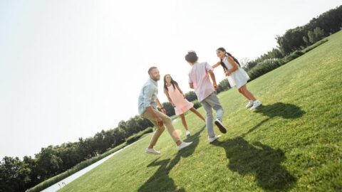Glückliche junge Familie, die spielt und lächelt, während sie ihre Freizeit im Freien im Park verbringt
