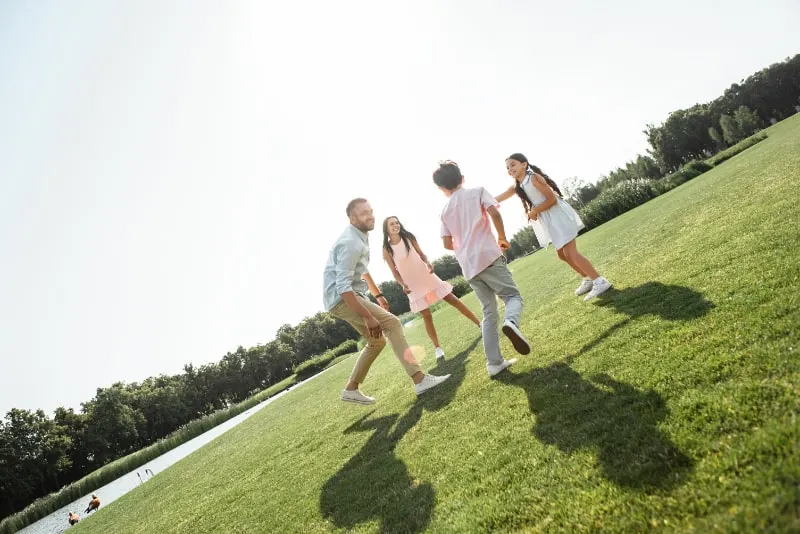 Glückliche junge Familie, die spielt und lächelt, während sie ihre Freizeit im Freien im Park verbringt