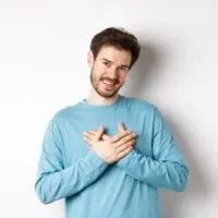 Porträt eines jungen gutaussehenden Mannes mit Bart, der die Hände am Herzen hält und sich bedankt und an einen angenehmen Moment denkt-min