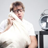 Schlafender Mann, der ein Kissen mit großer Uhr neben sich hält