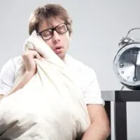 Schlafender Mann, der ein Kissen mit großer Uhr neben sich hält