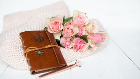 Rosa Rosen und ein Ledernotizbuch auf einer rosa Decke